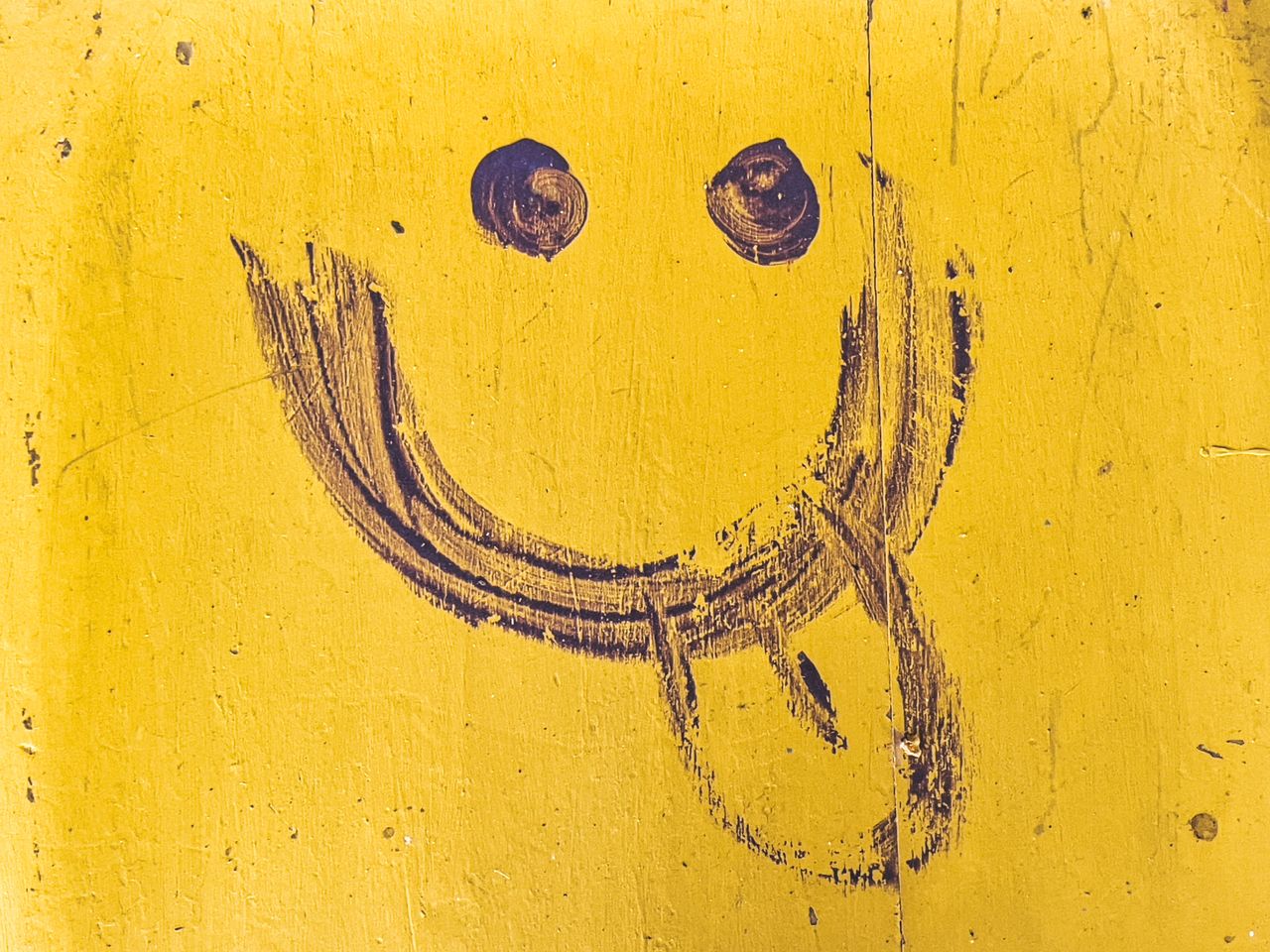 close up of a funny hand drawn smiley face on a yellow wall with textu