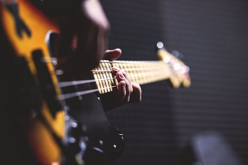 Person Playing Sun Burst Electric Bass Guitar in Bokeh Photography