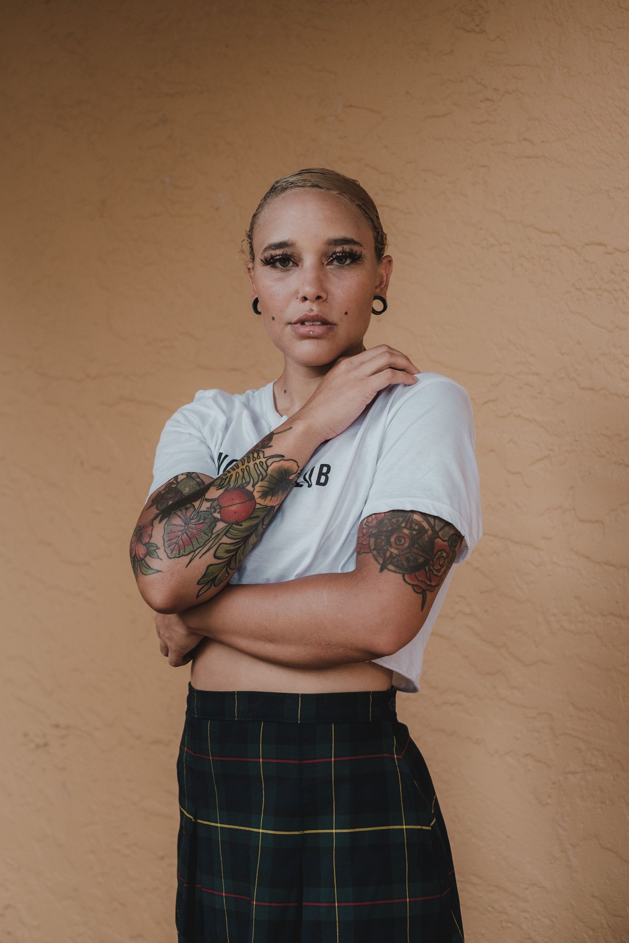 Stylish tattooed woman poses confidently indoors, showcasing fashion and personal expression.