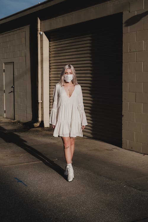 A Woman in White Long Sleeve Dress Standing Near Brown Brick Wall