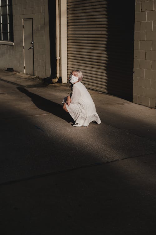 A Woman in White Dress Wearing Face Mask Sitting on Pavement