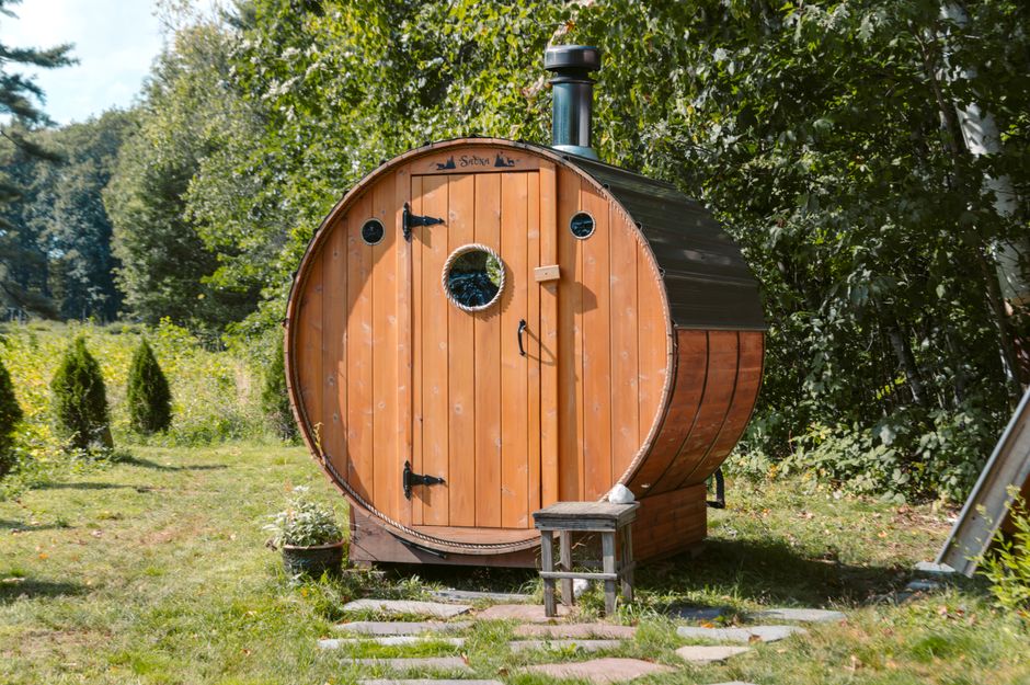 A charming barrel-shaped wooden sauna nestled among green foliage in a tranquil garden setting.