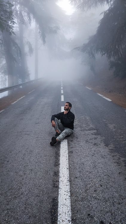 A Man Sitting Alone on a Foggy Road