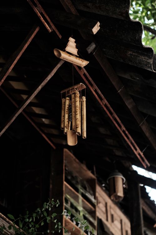 Free Bamboo wind chime hanging under a rustic wooden roof, creating a serene atmosphere. Stock Photo