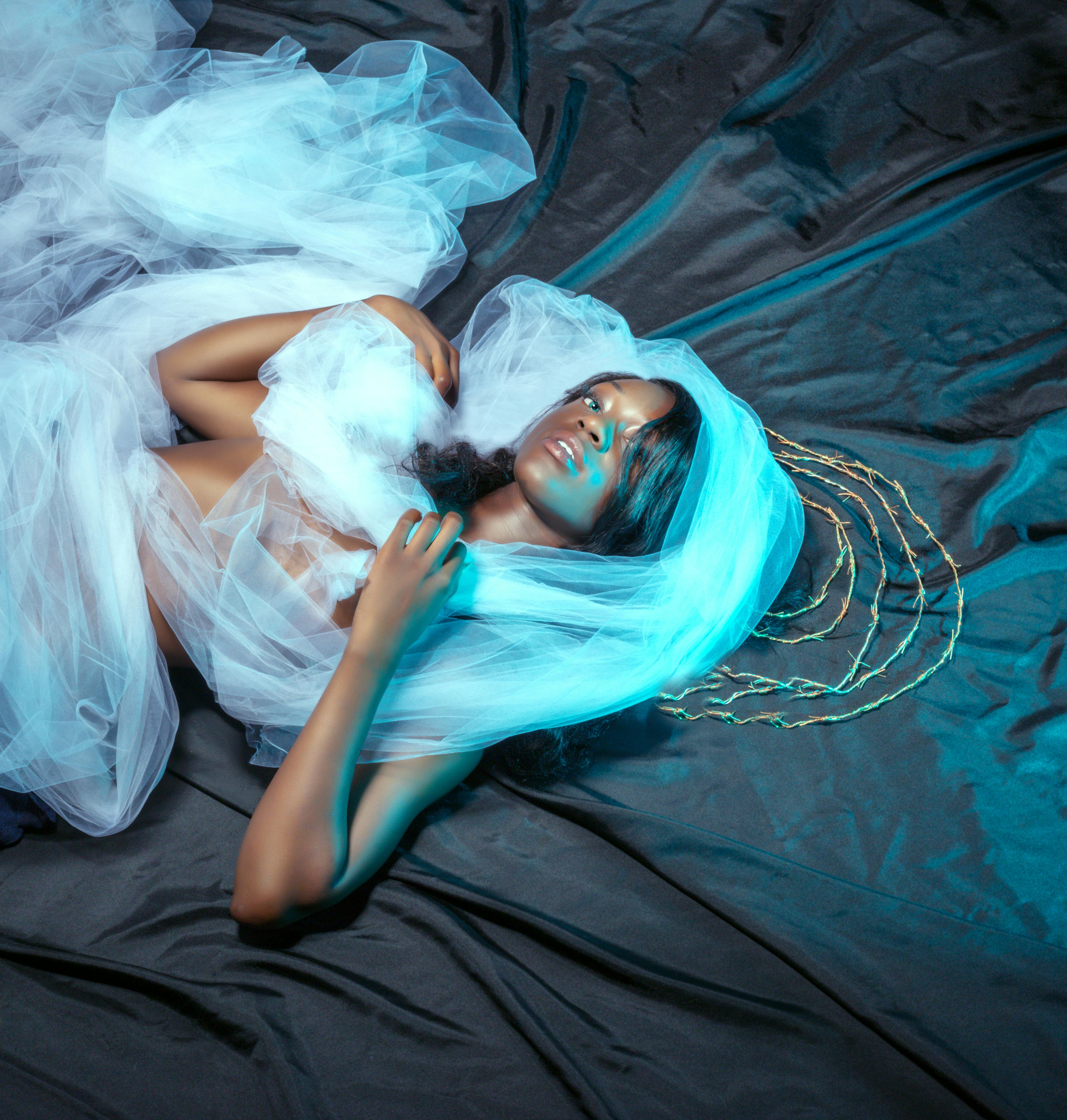 在优雅的蓝色灯光下，一位女士身着空灵的分层面料，艺术镜头捕捉着她散发的魅力