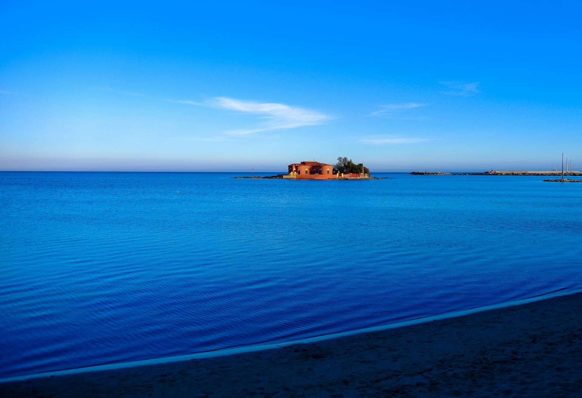 Tranquil island house surrounded by vibrant blue ocean under a clear sky. Perfect for travel inspiration.