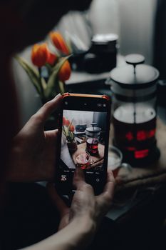 A cozy indoor scene capturing a French press with tea and tulips using a smartphone.