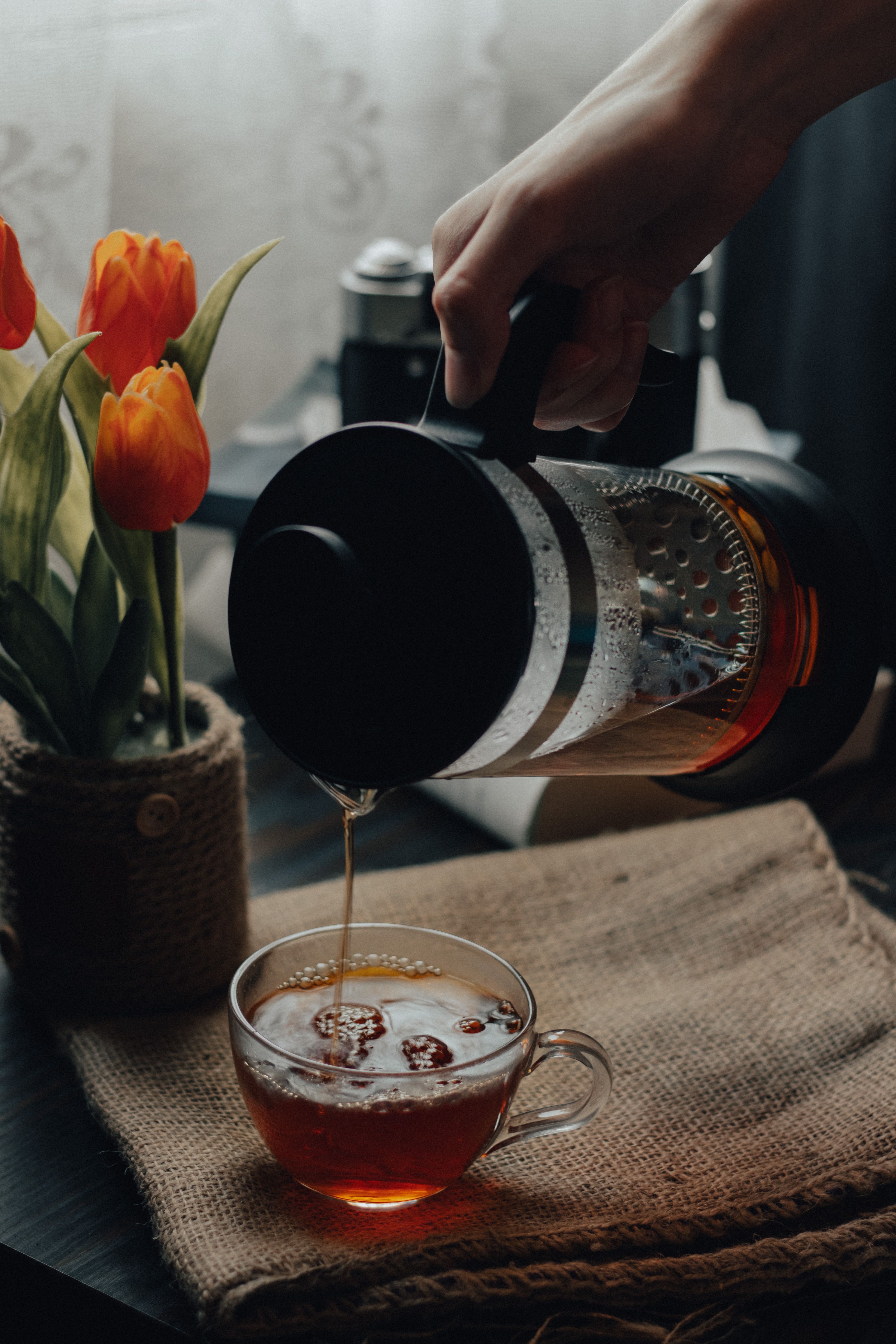 A warm, rustic scene with tea pouring from a French press beside vibrant tulips.