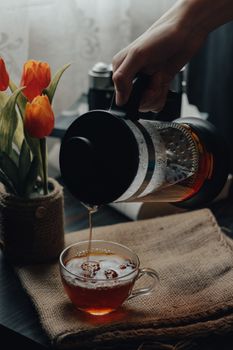 A warm, rustic scene with tea pouring from a French press beside vibrant tulips.