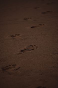 A series of human footprints trailing through sand, symbolizing a journey.