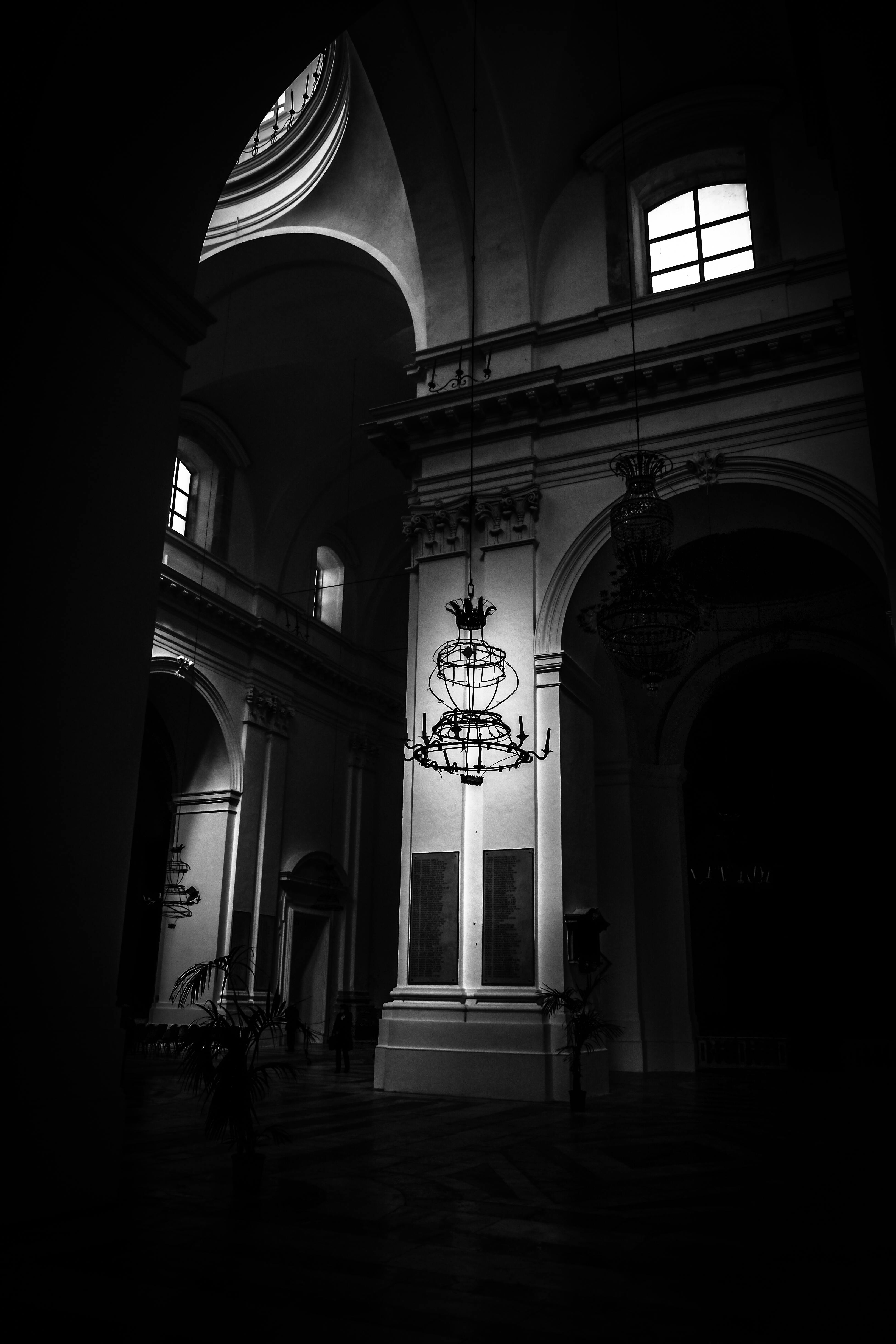 这张引人入胜的黑白照片展现了一座大教堂内部宏伟而阴暗的景象，配有复杂的拱门和枝形吊灯