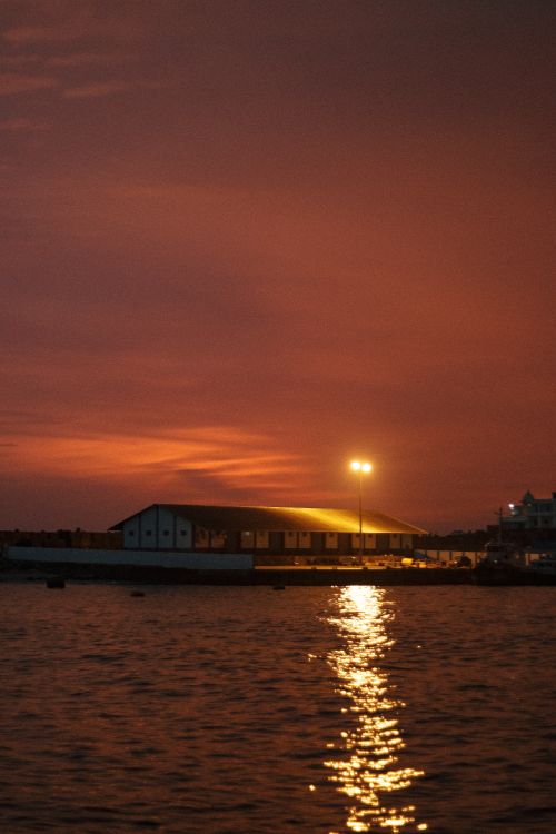 Free A tranquil lakeside building reflecting in the calm water at dusk, illuminated by warm streetlights. Stock Photo