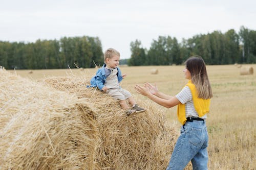 Woman Standing in Front of a Boy Sitting on a Hay Bale