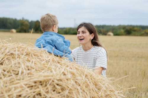 A Woman in White and Black Stripe Shirt Smiling at a Child in Denim Shirt