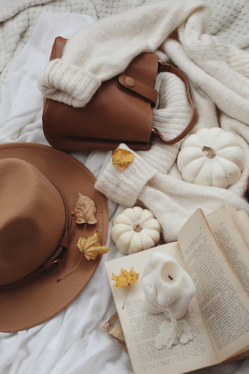 Close up view of autumn leaves, brown hat and bag, book and candles