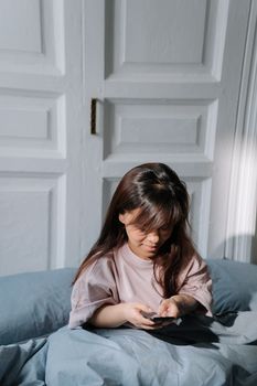Asian woman with dwarfism using smartphone in a sunlit bedroom, promoting technology and everyday life.