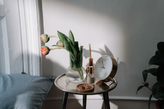Minimalist side table with vase of tulips and golden clock in soft daylight.