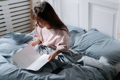 Free Woman with dwarfism reading book in bed Stock Photo