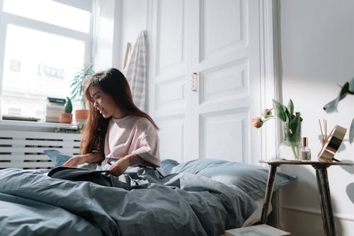 Free Woman with dwarfism reading book in bed Stock Photo