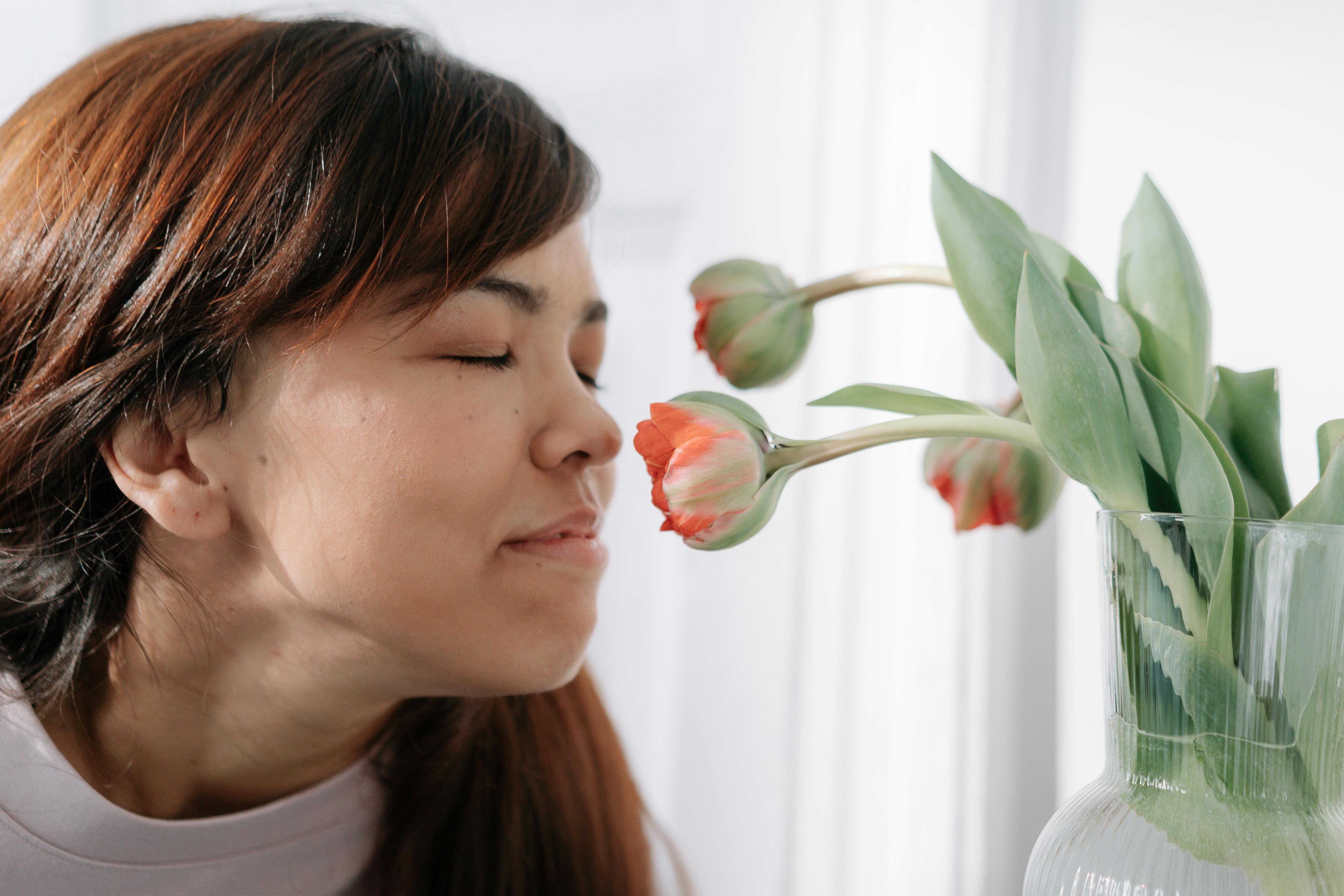 A woman with brown hair enjoys smelling tulips indoors, eyes closed in contentment.
