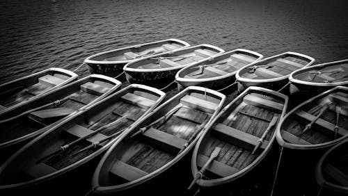 Gray Scale Photography of Wooden Rowboats on Body of Water