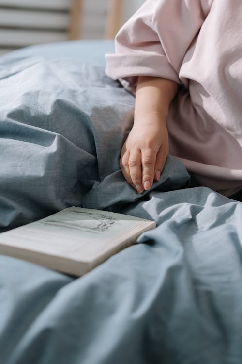 Free Female hand laying on duvet close to book Stock Photo