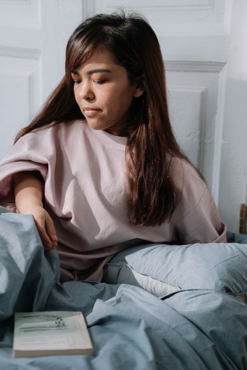 Free Woman sitting in bed in a relaxed mood, morning light, holding a book. Stock Photo