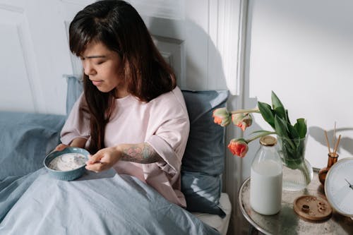 Woman eating cereal with milk sitting in a bed