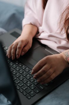 Close-up of a woman typing on a laptop in a casual indoor setting, focusing on hands and technology use.