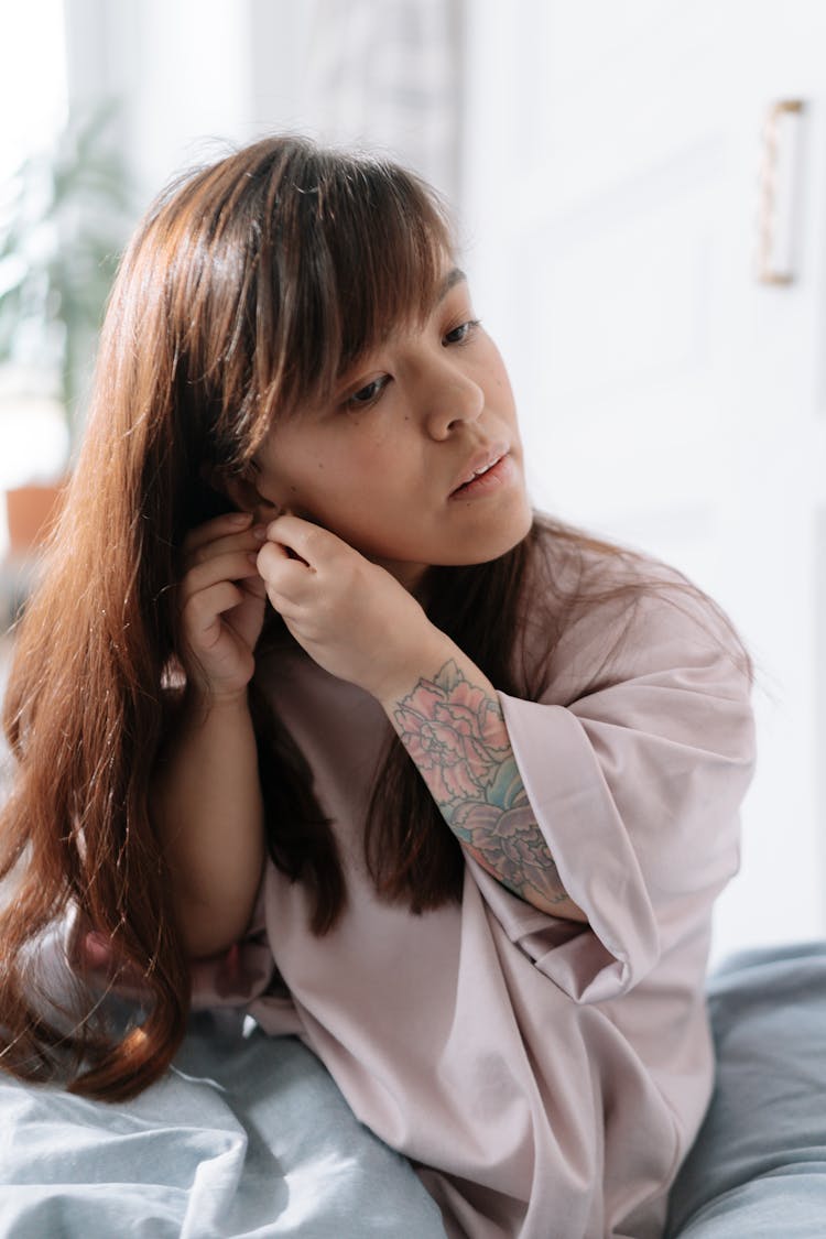 Girl With Dwarfism Sitting In Bed And Touching Her Right Ear With Hands