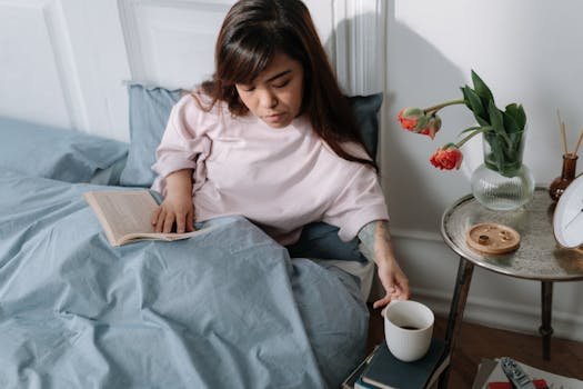 Woman enjoying a relaxing morning in bed, reading a book and sipping coffee.