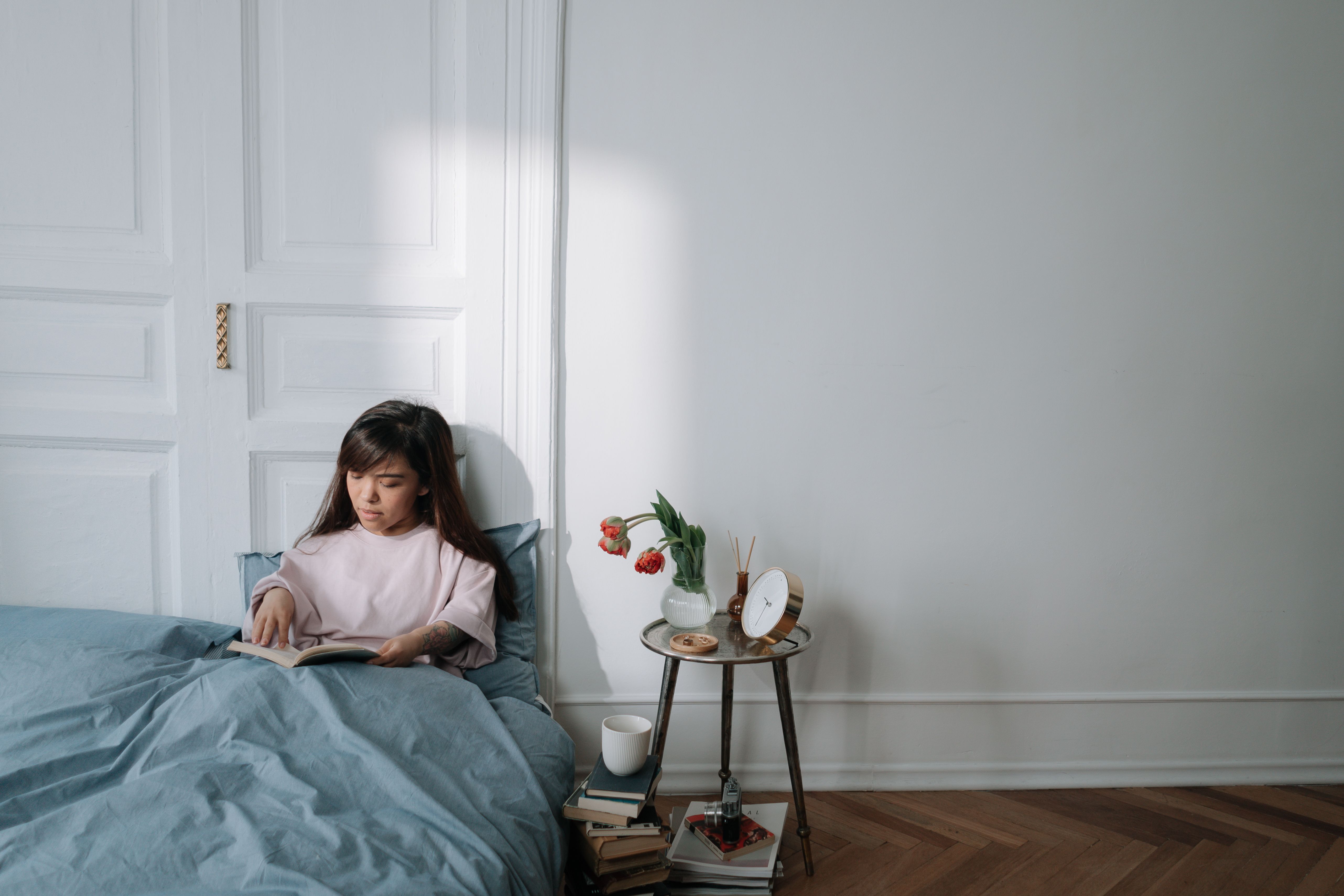 Woman sitting on a bed reading a book in a serene bedroom with morning light.