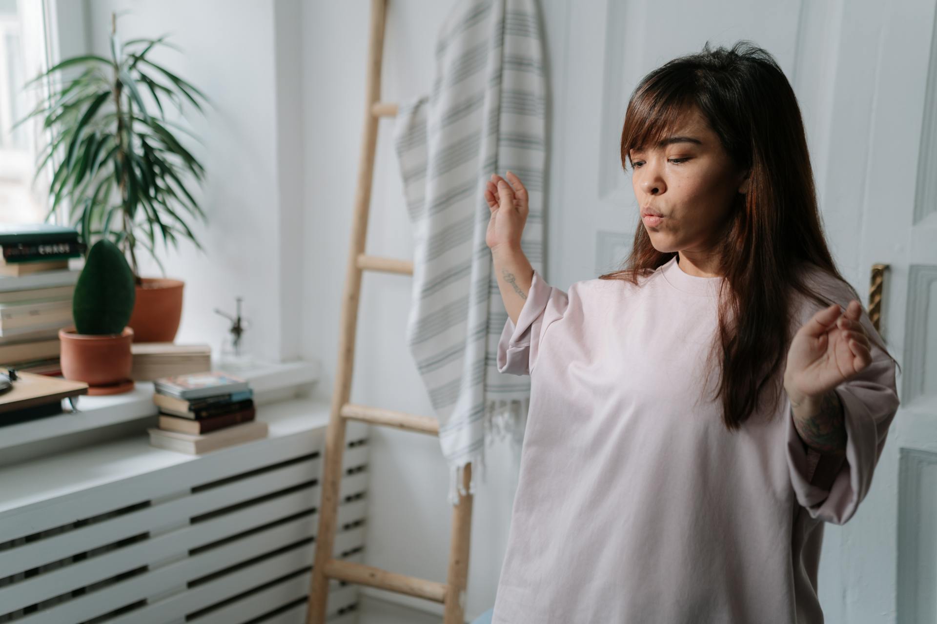Woman in an oversized shirt enjoying a peaceful moment in her cozy, plant-filled bedroom.