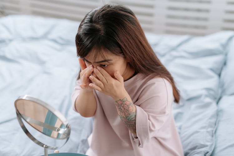 Dwarf Young Woman Sitting In Bed And Rubbing Face Cream Looking To Mirror