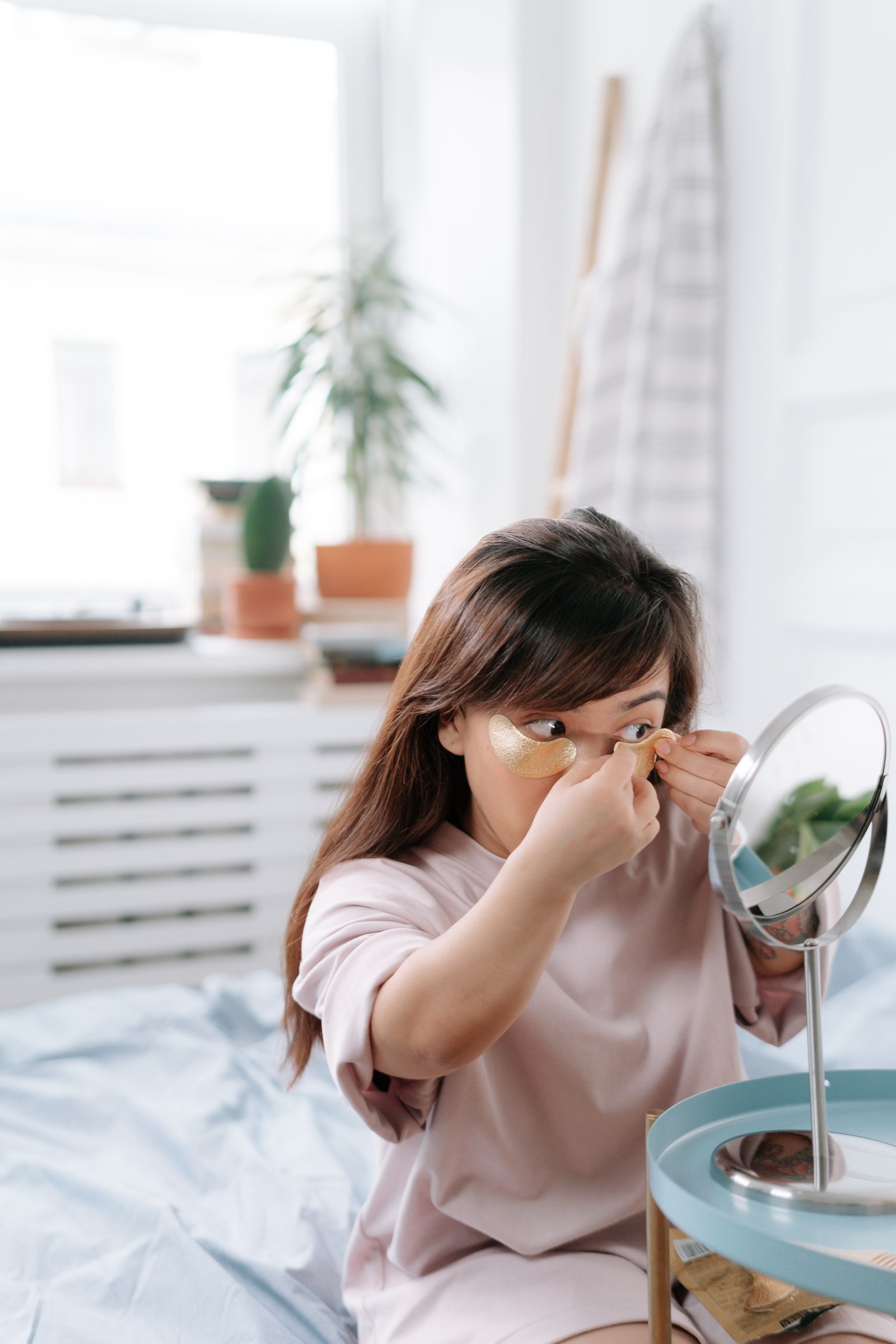 Woman applying an under-eye patch under her eyes in a mirror during a morning skincare routine