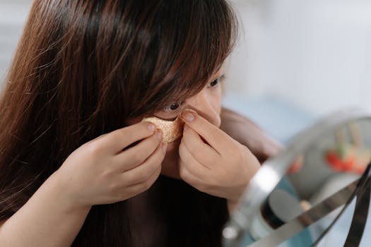 Young woman applying eye patch as part of her daily skincare routine in front of a mirror.