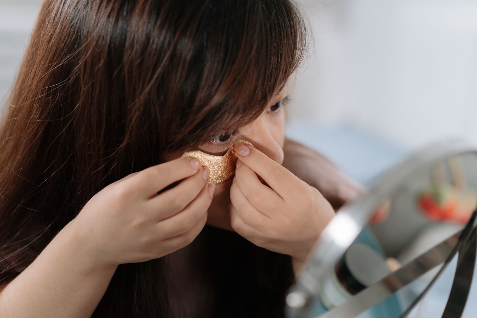 Close-up of a woman pressing a gel eye patch into place near a mirror