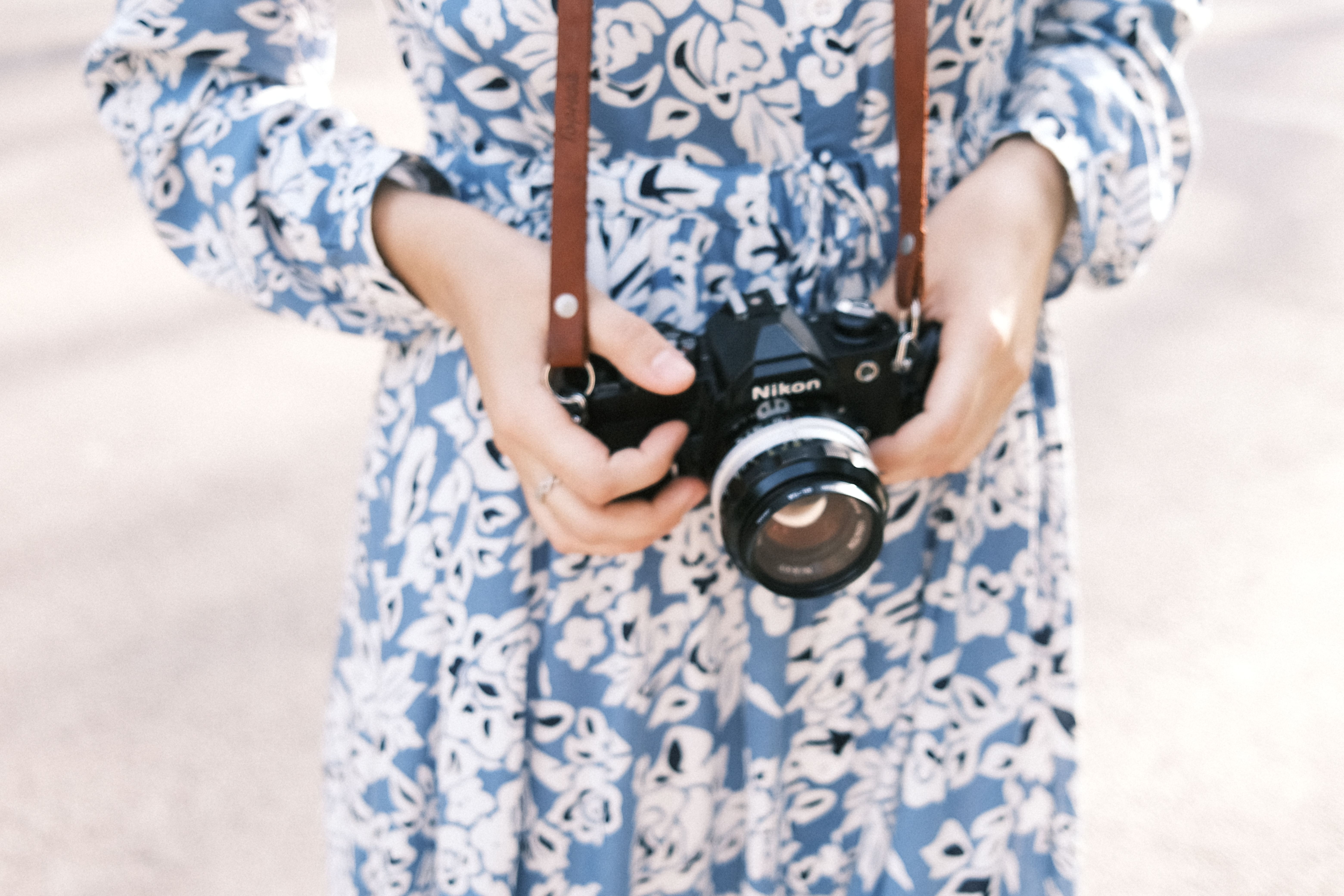 A woman in a floral dress holds a vintage film camera outdoors on a sunny day.