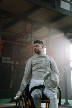 Wheelchair fencer in gear, focused and ready in an indoor arena.