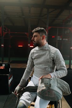 Male athlete in wheelchair fencing gear, indoors, ready for a match.