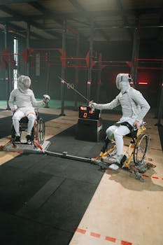 Two athletes engage in wheelchair fencing, showcasing dynamic sports action indoors.
