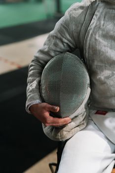 Close-up of a fencer holding their mask in an indoor training setting, emphasizing readiness.
