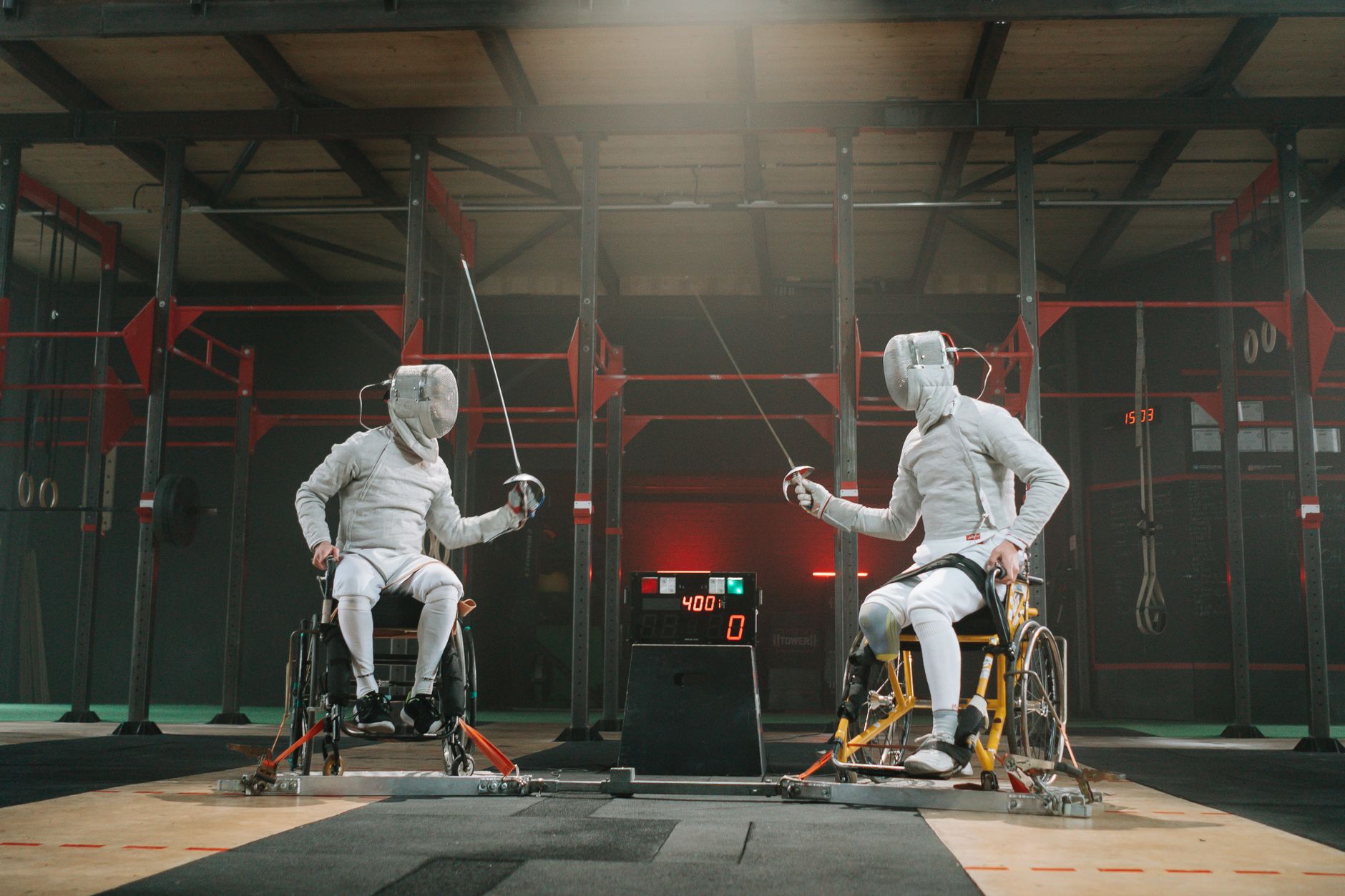 Two wheelchair fencers practice indoors, showcasing competitive sportsmanship.