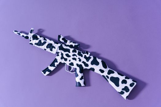 A toy gun in a cow print camouflage design lies on a vibrant purple surface, casting a shadow.