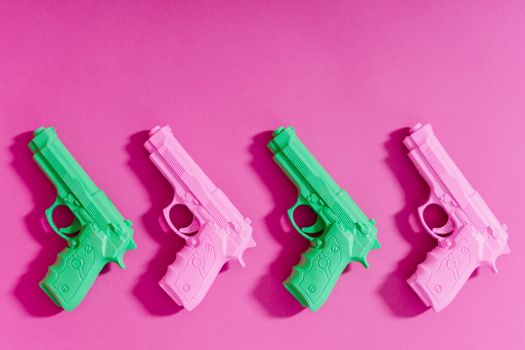 Brightly colored toy guns arranged on a vivid pink backdrop, creating a playful conceptual theme.