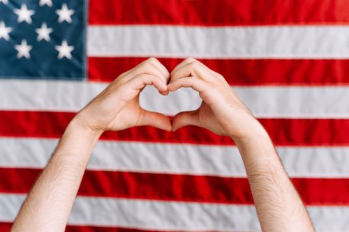 Free Hands forming a heart shape in front of the American flag, symbolizing love and patriotism. Stock Photo