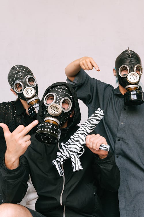 Three Men in Studded Gas Masks Posing with a Toy Gun