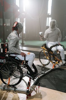 Two athletes engage in an intense wheelchair fencing match indoors.