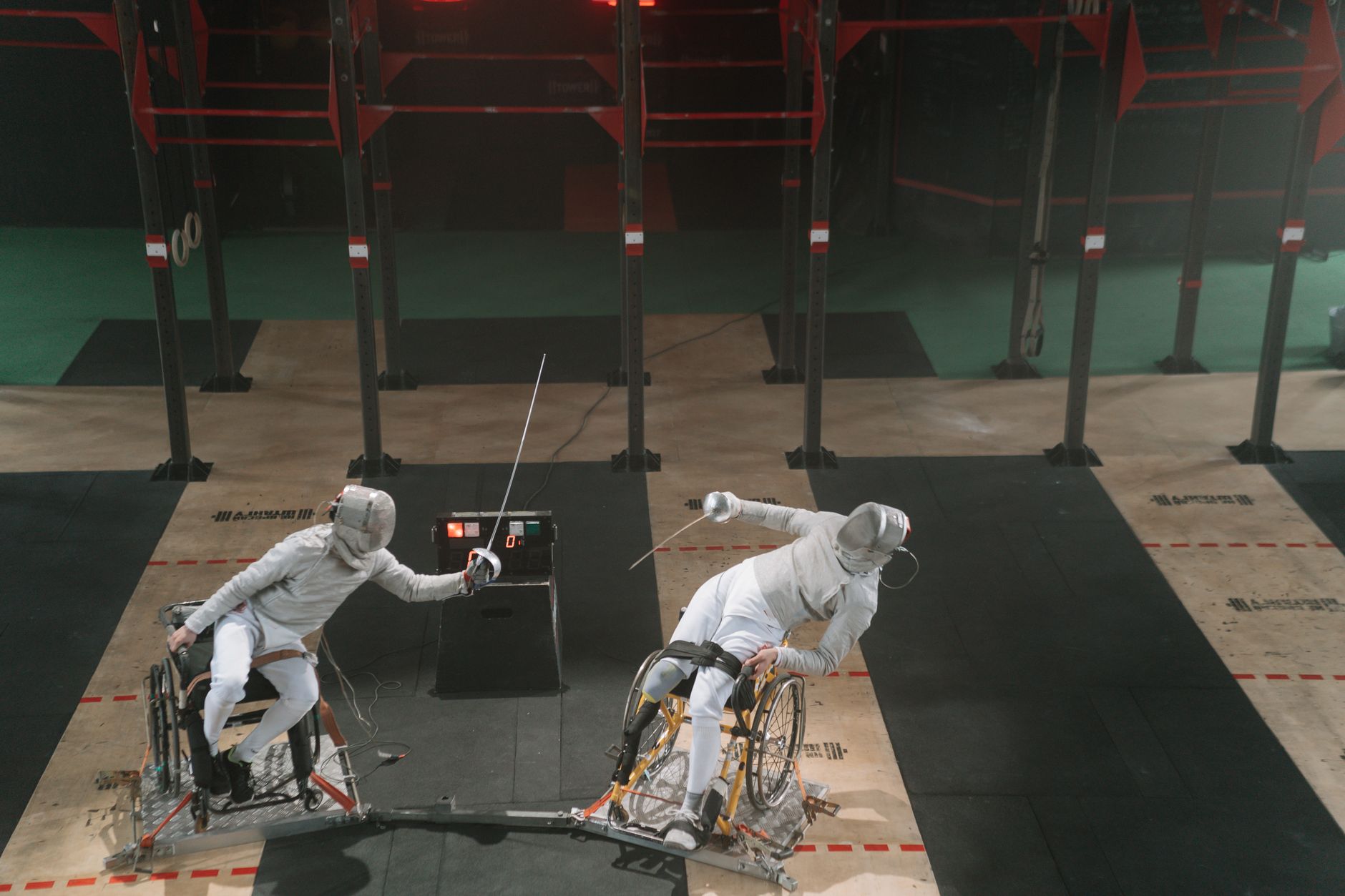 Two fencers in wheelchairs engage in a competitive match indoors, showcasing adaptive sports.