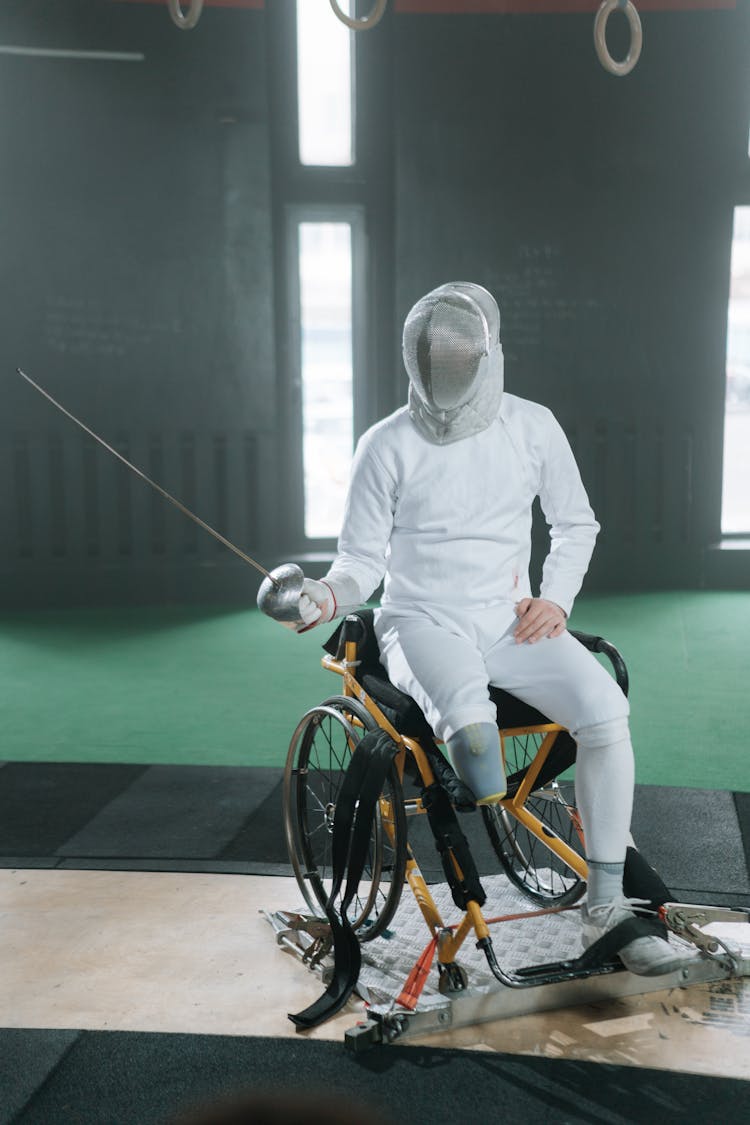 A Side View Of A paralympic athlete Sitting On Wheelchair And Holding A Foil